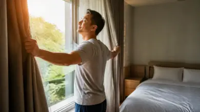 Mann öffnet morgens die Vorhänge für natürliches Licht und einen stabilen Tagesrhythmus