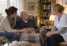 Älterer Mann mit Angehöriger und Pflegekraft im Gespräch zu Hause